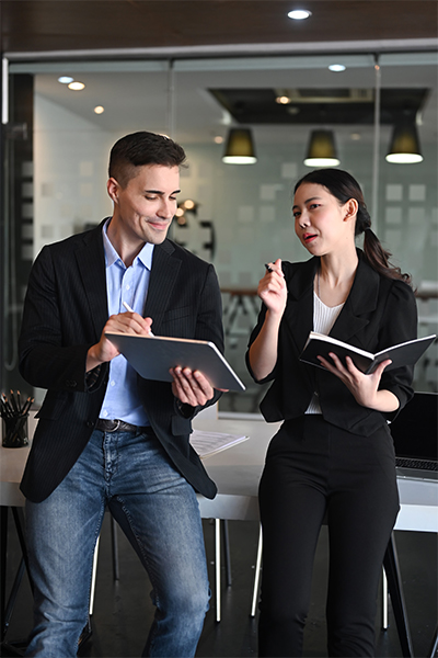 professionally dressed man and woman standing in office space with notebook and tablet professionally dressed man and woman standing in office space with notebook and tablet